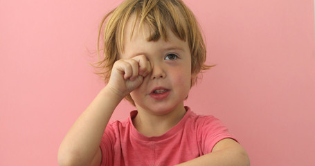 Adorable little boy in pink t-shirt rubbing eye looking sleepy on pink background