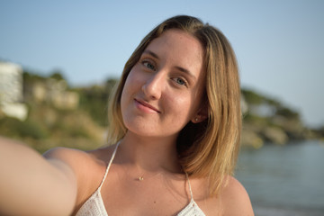Close up portrait of a girl smiling and taking selfie on the beach