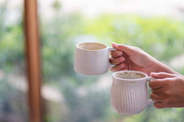 Closeup image of hands holding two white cups of hot coffee with blurred nature background