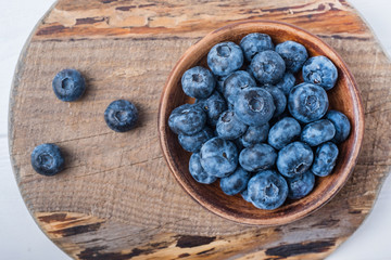 Blueberries in small clay bowl on white wooden table.