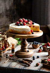 Homemade raspberry sliced biscuit cake with white cream and berries on top on wooden cake stand