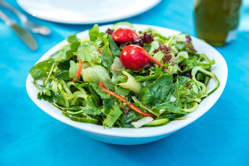 Greek, Mediterranean or Aegean Green fresh vegetarian Salad on the table in Fish Restaurant. Green Salad in bowl with olive oil at Beach Fish Restaurant in Greece or Turkey.