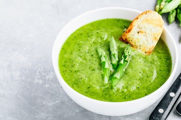 Asparagus cream soup with croutons on gray stone background.