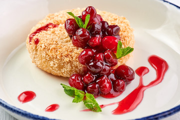 baked camembert with cranberry jam and mint leaves at white wooden table top. fried camembert with berry sauce is traditional french cuisine dessert