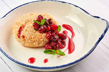baked camembert with cranberry jam and mint leaves at white wooden table top. fried camembert with berry sauce is traditional french cuisine dessert