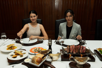 Fototapeta na wymiar Couple of two 2 Asian Woman Black hair having Lunch Steak grill salmon bread Dinner of Western food in fusion restaurant cafe and eat alone. Concept enjoy eating tom boy best friends and serve each