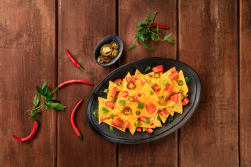 Mexican nachos, shot from the top with a cheese sauce, chili and jalapeno peppers, tomatoes, and cilantro, on a dark rustic wooden background with a place for text