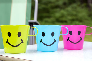 three plastic cups with an attractive face with a smile are standing on a picnic table in nature