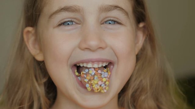 A child is smiling with a mouth full of candy. Little girl eating candy. Child eating chicle. Close up portrait silly girl with wavy hair sticking out tongue shaped candy pieces on tip.