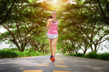 woman jogging exercise on the roas in public park trees, workout under shade of the trees forest...