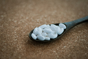 White pharmaceutical pills and medicines in the wooden spoon on a brown cork background....
