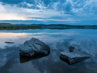 Calm, serenity, meditation concept. Sunset on the lake, stones in the water in the foreground,...