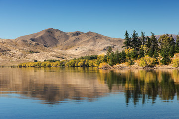 Lake in the dry landscape with trees and mountains. Horizontal image with reflections in the water. Beautiful background photography concept.