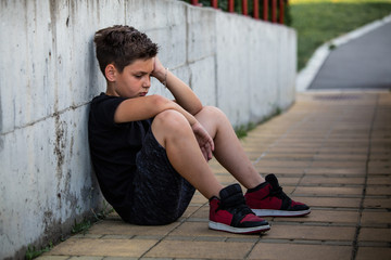 Boy sitting and thinking about something sad. Isolation and bullying concept. Kid sad and unhappy, child was crying, upset, feel sick