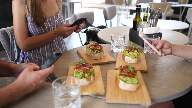 Group Of Friends Taking Photo Of Food With Smartphones.