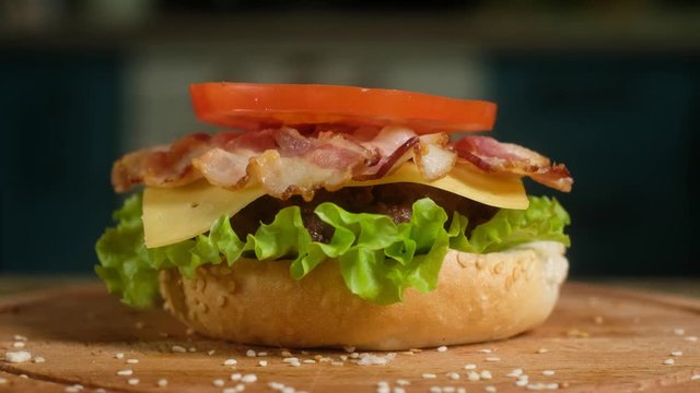 In the frame consistently appear bun, green salad, fried cutlet, slice of cheese, crispy bacon, tomato, onion. The Assembly of the Burger.