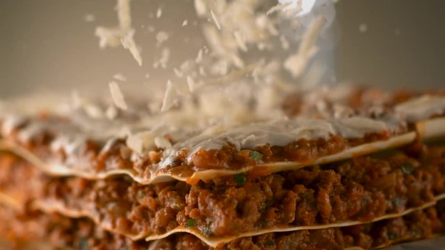 Appetizing meat lasagna is sprinkled with pieces of grated cheese. Parmesan.Very beautiful studio shot. Slow motion. Camera Phantom Flex 4K.