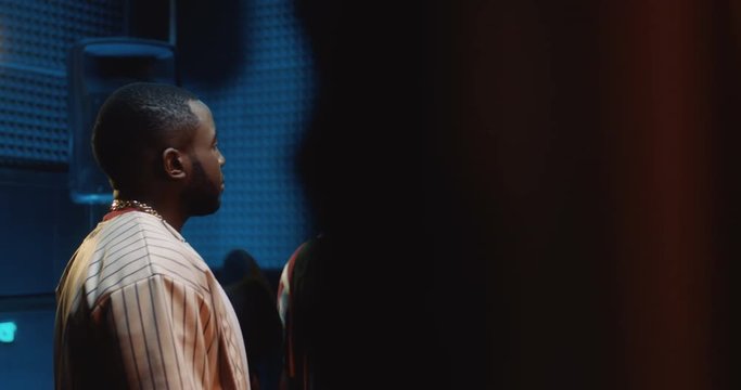 Two young African American stylish guys rappers talking and deciding something while standing in the sound studio at the mic and getting ready to record a song.