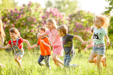 A group of happy children of boys and girls run in the Park on the grass on a Sunny summer day . The concept of ethnic friendship, peace, kindness, childhood