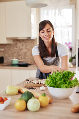 Beautiful hardworking housewife taking salad from bowl while standing in kitchen. Home made dinner preparation concept.