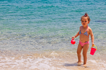 A little cute baby girl is playing on a beach near the sea on holiday