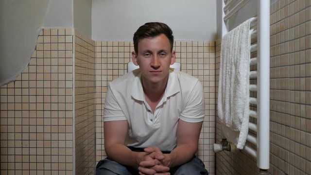 Young man sitting on a toilet, close-up
