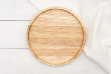 Empty round wooden plate with white tablecloth on white wooden table. Top view image.
