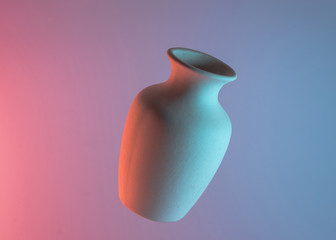 White plain ceramic vase in air against colored blue and pink backdrop