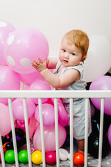 Little cute baby girl princess infant 1-2 year standing and playing on bed at home decorated colored balloons for birthday party. Happy baby for a holiday. Celebration first year concept.