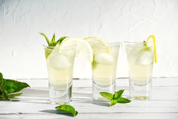 small cups of limoncello liqueur decorated with mint and lemon slices on a white wooden background