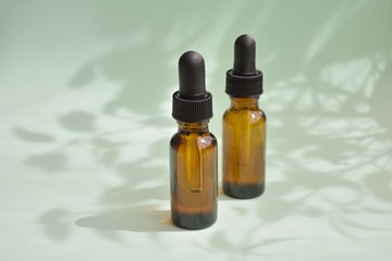 Aromatherapy, phytotherapy, beauty from nature, dropper bottles with essential or cosmetic oils on green background with tree leaves shadows.