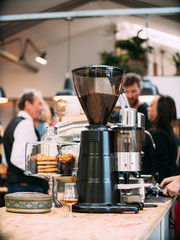Coffee grinder with espresso machine in a crowded bar.