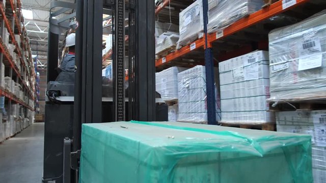 A forklift with a box rides along the stands at the warehouse. 4K Slow Mo
