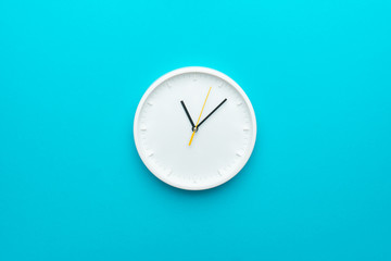 White wall clock with yellow second hand hanging on the wall. Minimalist flat lay image of plastic wall clock over blue turquiose background with copy space and central composition. - obrazy, fototapety, plakaty