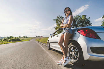 Girl in the bright sun on the road with cabriolet car. The concept of adventure and travel alone....