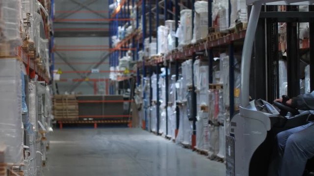 The worker moves on a lifting machine through a logistic warehouse. 4K Slow Mo