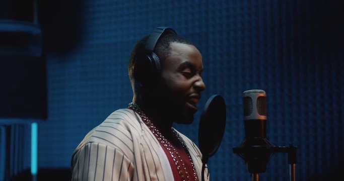 Close up of the young stylish African American male r'n'b singer finishing to record a song in the sound studio and taking off headphones.