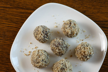 Homemade candy in the form of balls of dried fruit and walnut on a white plate on the table. Healthy food without sugar and gluten.