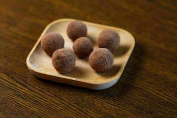 Homemade candy in the form of balls of dried fruit and cocoa powder on a wooden plate on the table. Healthy food without sugar and gluten.