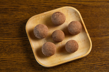 Homemade candy in the form of balls of dried fruit and cocoa powder on a wooden plate on the table. Healthy food without sugar and gluten.