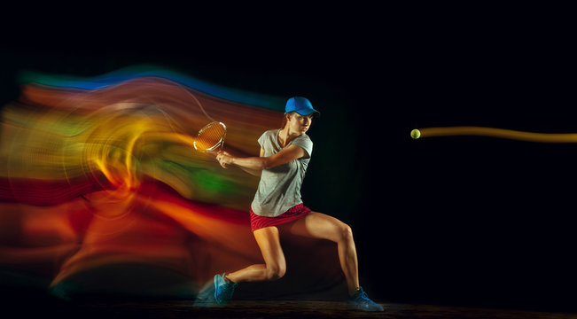 One caucasian woman playing tennis isolated on black background in mixed and stobe light. Fit young female player in motion or action during sport game. Concept of movement, sport, healthy lifestyle.