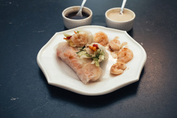 Spring rolls on a white plate with peanut sauce. Vietnamese snacks are on the dark table