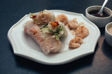 Spring rolls on a white plate with peanut sauce. Vietnamese snacks are on the dark table