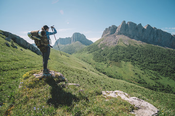 молодая женщина с туристическим рюкзаком смотрит на горную вершину в солнечный летний день