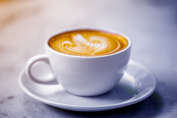 The  white ceramic cup of hot capuccino coffee on the wooden table in the restaurant or coffee shop with flare in the natural light , violet or blue light theme. 