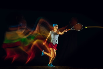 Fototapeta premium One caucasian woman playing tennis isolated on black background in mixed and stobe light. Fit young female player in motion or action during sport game. Concept of movement, sport, healthy lifestyle.