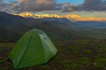 Sunrise view of Mount Denali - mt Mckinley peak with alpenglow during golden hour with green camping tent in the foreground from Stony Dome overlook.