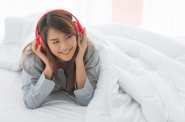 Young happy Asian woman lie down on bed and listening music in modern bedroom