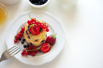 Stack of pancakes (syrniki) with strawberry, red currant and blueberries on white backgraund. Soft focus. Healthy eating concept