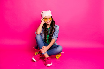 Full length body size photo cheer beautiful little she her curly lady sit nowadays modern hobby long board legs crossed wear yellow sun specs hat casual jeans denim jacket isolated pink background